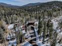 Aerial view of the home nestled in a forested area with a long driveway and surrounding mountains at 10438 Sunlight Ln, Conifer, CO 80433
