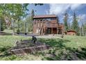 Spacious backyard with a multilevel deck, a lush lawn, mature trees, and a charming garden area at 10438 Sunlight Ln, Conifer, CO 80433