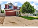 Two-story home featuring a red exterior, spacious driveway, two-car garage, and well-maintained lawn at 5558 Malta St, Denver, CO 80249