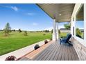 Inviting covered porch with wood flooring and seating overlooks a spacious, lush front yard at 3047 Deer Creek Ranch Loop, Parker, CO 80138