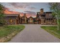 Beautiful home featuring a stone and wood exterior, porte-cochere, and circular driveway at sunset at 220 Cottonwood Cir, Breckenridge, CO 80424