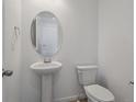 Modern powder room with pedestal sink, oval mirror, and white commode at 45909 Wood Thrush Ave, Bennett, CO 80102