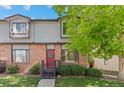 Charming townhome with brick facade, red door with wreath, well-maintained lawn, and mature shade tree at 10693 W 63Rd Dr # 106, Arvada, CO 80004