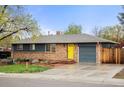 Single-story brick home with a well-kept lawn, a driveway, and a pop of color from the yellow front door at 6742 Marshall St, Arvada, CO 80003