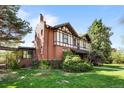 Exterior view of a well-maintained two-story Tudor-style home with brick siding, green roof and a lush lawn at 1317 Birch St, Denver, CO 80220