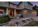 Inviting home entrance with a covered porch, stone accents, lush greenery, and an attached two-car garage at 1805 Parkdale N Cir, Erie, CO 80516