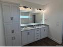 Bathroom with double sinks, granite countertop, shaker cabinets, and a large, illuminated mirror at 59440 E 56Th Ave, Strasburg, CO 80136