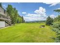 Expansive green backyard featuring a fire pit and stunning views of distant mountains under a bright blue sky at 7614 Malamute Dr, Evergreen, CO 80439