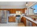 Well-lit kitchen featuring stainless steel appliances, wood cabinets, and a sink with a backyard view at 12432 Bellaire St, Thornton, CO 80241
