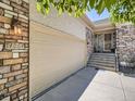 Home exterior featuring a light colored two car garage, stone accents, and front door entry at 14064 E Whitaker Dr, Aurora, CO 80015
