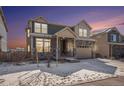 Two-story home with stone facade, attached garage, and snowy front yard with sunset at 16278 E 111Th Pl, Commerce City, CO 80022