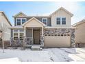 Charming two-story home with a stone facade, attached garage, covered entry, and snow-covered yard at 16278 E 111Th Pl, Commerce City, CO 80022