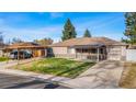Attractive single-story home with a carport, covered porch, and attached garage, framed by mature trees at 724 Ursula St, Aurora, CO 80011