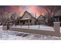 Charming two-story home featuring a well-maintained lawn and secure black metal fence with winter landscape at 1751 Clermont St, Denver, CO 80220