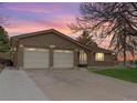 Charming brick home featuring a two-car garage and an inviting front entrance at sunset, perfect for suburban living at 2696 S Yukon Ct, Lakewood, CO 80227
