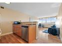 Open kitchen with stainless steel dishwasher next to a modern, well-lit living room with hardwood floors at 1196 N Grant St # 407, Denver, CO 80203