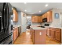 Spacious kitchen with wood cabinets, center island, hardwood floors, and modern black appliances at 11034 Nome St, Commerce City, CO 80640