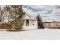 A quaint home with a charming front porch, nestled in a snow-covered yard, with mature trees and a serene setting at 1827 W 47Th Ave, Denver, CO 80211