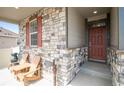 Charming front porch with stone accents, cozy seating, and a welcoming entryway with a dark red front door at 7108 Morrison Dr, Frederick, CO 80530