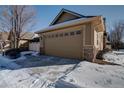 Attached garage with stone accents and snowy driveway at 8588 W Quarles Pl, Littleton, CO 80128