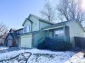 Two-story light green house with a two-car garage, snowy yard, and trees at 3802 Desert Willow Ave, Broomfield, CO 80020