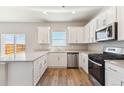 Well-lit kitchen with white cabinets, stainless steel appliances, quartz countertops and wood laminate floors at 48220 Shetland Dr, Bennett, CO 80102