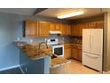 Well-lit kitchen with breakfast bar, oak cabinets, granite counters, and white appliances at 12304 W Cross Dr # 304, Littleton, CO 80127