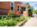 Inviting brick home with a covered front porch and a beautiful garden with lush greenery and vibrant pink flowers at 22 E Bayaud Ave, Denver, CO 80209