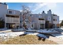 Exterior view of a multi-story condominium with a balcony, stairs, and lawn covered in snow at 7665 E Eastman Ave # 107B, Denver, CO 80231