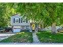 Charming home with gray siding, dark shutters, yellow door, attached garage, and mature trees in a well-manicured yard at 8710 Alta Vista Dr, Arvada, CO 80004