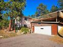 This exterior elevation showcases a two-story home, driveway, and an attached garage with a wooden deck above at 3841 Myers Gulch Rd, Kittredge, CO 80457