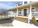 Inviting front porch with gray siding, white columns and railings, and wooden steps leading to a dark gray front door at 1465 Arabian Trl, Elizabeth, CO 80107