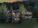 Exterior of a gray stone home with lit windows during sunset amongst lush trees at 2191 Baldy Ln, Evergreen, CO 80439