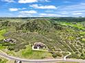 Expansive aerial view showcasing a large stone house nestled in a lush green landscape with rolling hills at 4222 Serenade Rd, Castle Rock, CO 80104