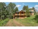 Charming two-story cabin with a welcoming front porch and balcony nestled among lush greenery and mature trees in a serene setting at 20033 Silver Ranch Rd, Conifer, CO 80433