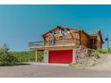 Log cabin with a spacious balcony above a red garage door, offering stunning views of the surrounding nature at 12135 Cochise Cir, Conifer, CO 80433