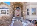 Close-up of a home's entryway featuring a stone archway, burgundy front door, and decorative planters at 6943 Saddleback Ave, Firestone, CO 80504