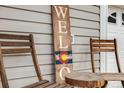 Inviting front porch featuring a rustic welcome sign, wooden chairs and a small accent table at 1495 Hummingbird Cir, Brighton, CO 80601