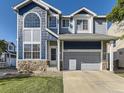 Charming two-story home boasts blue siding, stone accents, a manicured lawn, and an attached two-car garage at 9832 Kenton Cir, Commerce City, CO 80022