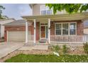 Close-up of a welcoming front porch with brick columns, a wooden door, and decorative plants at 4426 Windmill Dr, Brighton, CO 80601