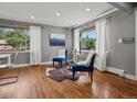Bright living room with hardwood floors, two blue chairs, large windows, and sheer curtains at 6943 Oak Way, Arvada, CO 80004