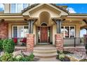Charming front porch with brick columns, manicured landscaping, and wooden front door at 9164 E Lost Hill Trl, Lone Tree, CO 80124