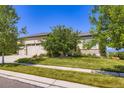Charming stucco home with a manicured lawn, mature trees, and a three-car garage under a blue sky at 15975 Quandary Loop, Broomfield, CO 80023