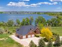 Aerial view of a brick home showcases a three-car garage and lush landscaping, near a serene lake at 2366 Shoreside Dr, Berthoud, CO 80513