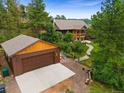 Wide aerial view of a brown home and a two-car garage surrounded by many trees at 776 Hilltop Rd, Palmer Lake, CO 80133