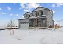 Two-story house with gray siding, stone accents, and a two-car garage in a snowy landscape at 25022 E 34Th Pl, Aurora, CO 80019