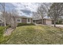 A single-story brick home features a well-maintained lawn, a two-car garage, and mature trees in the landscape at 8150 W Calhoun Dr, Littleton, CO 80123