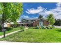 Inviting two-story home boasts a lush lawn, mature tree, and a charming brick and gray exterior at 10289 E Berry Dr, Greenwood Village, CO 80111