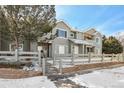 View of gray siding townhome exterior with a snow covered yard and low brick wall and white wooden fence at 912 S Yampa St # 208, Aurora, CO 80017