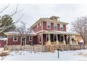 Red two-story home with a wrap-around porch and picket fence at 9112 E 29Th Pl, Denver, CO 80238